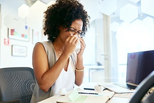 Sick employees blowing her nose at desk