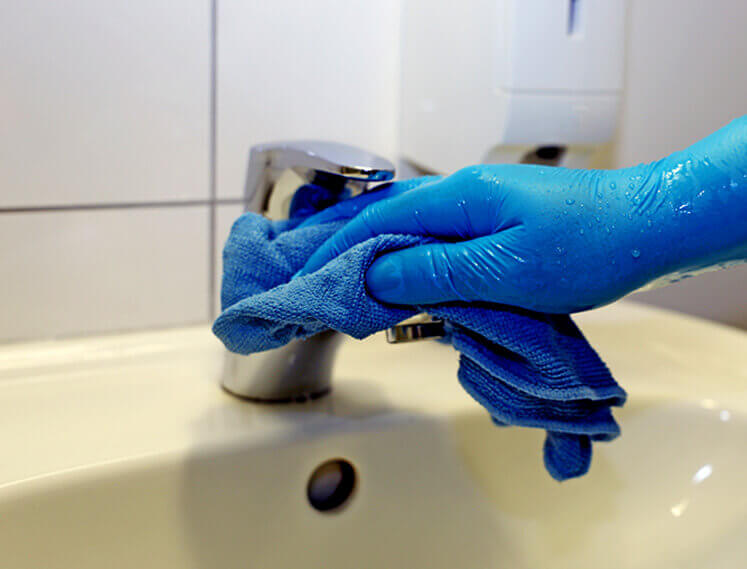Cleaning professionals hand with blue gloves cleaning a bathroom sink faucet