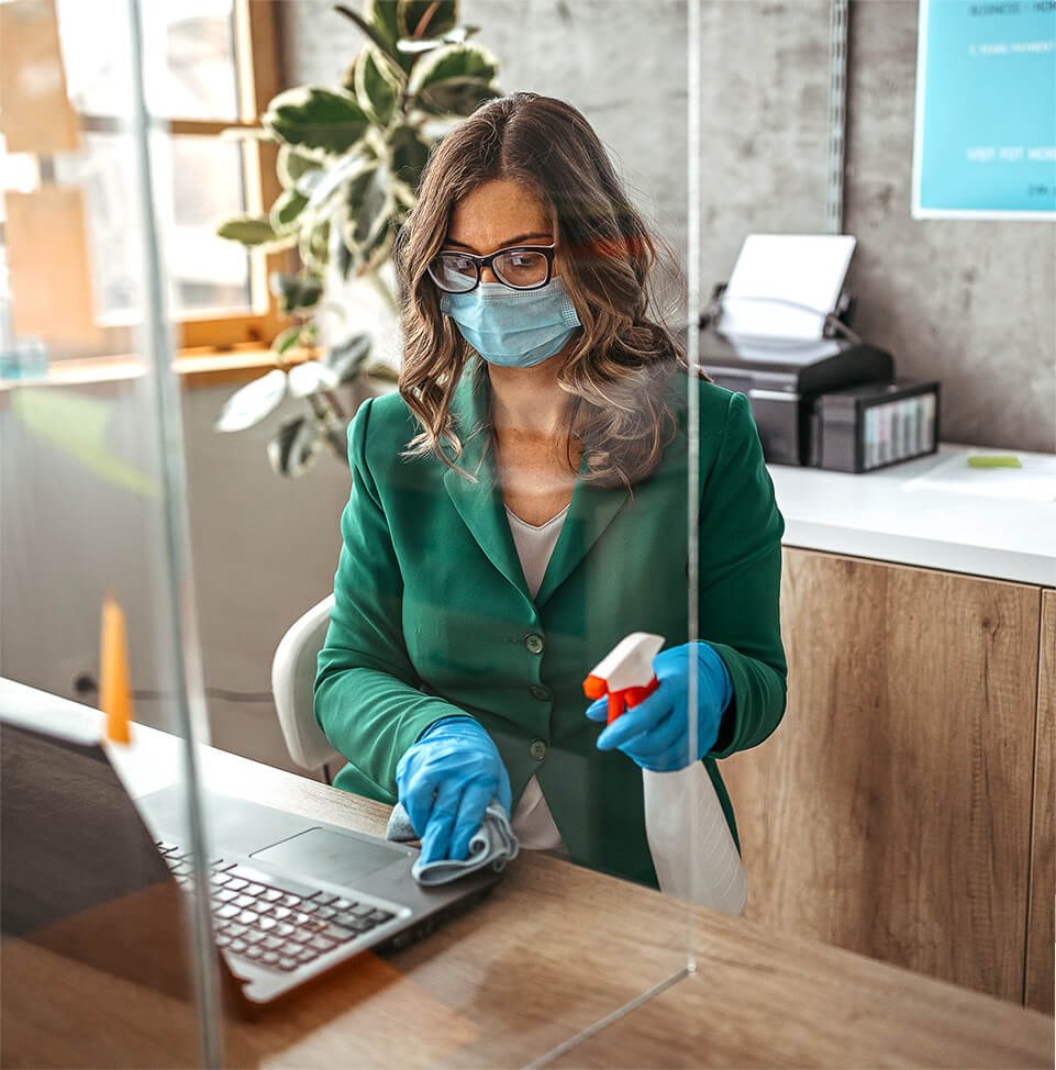 woman wearing mask while cleaning desk with glass divider