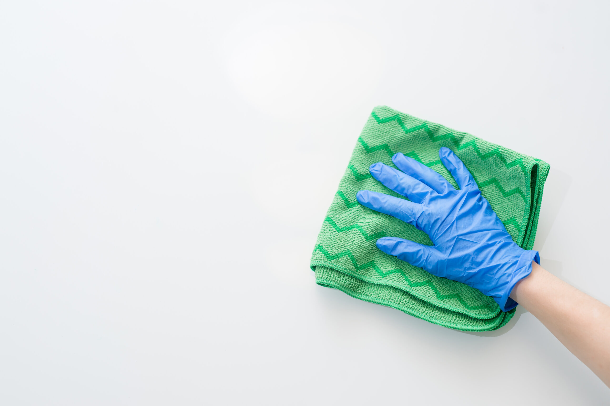 hand wiping surface with green wag and blue gloves