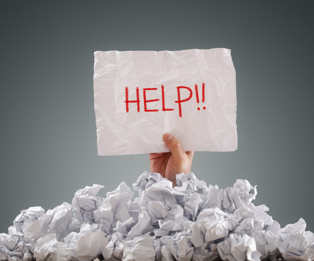 pile of paper balls with a hand extending out holding a sign that reads help