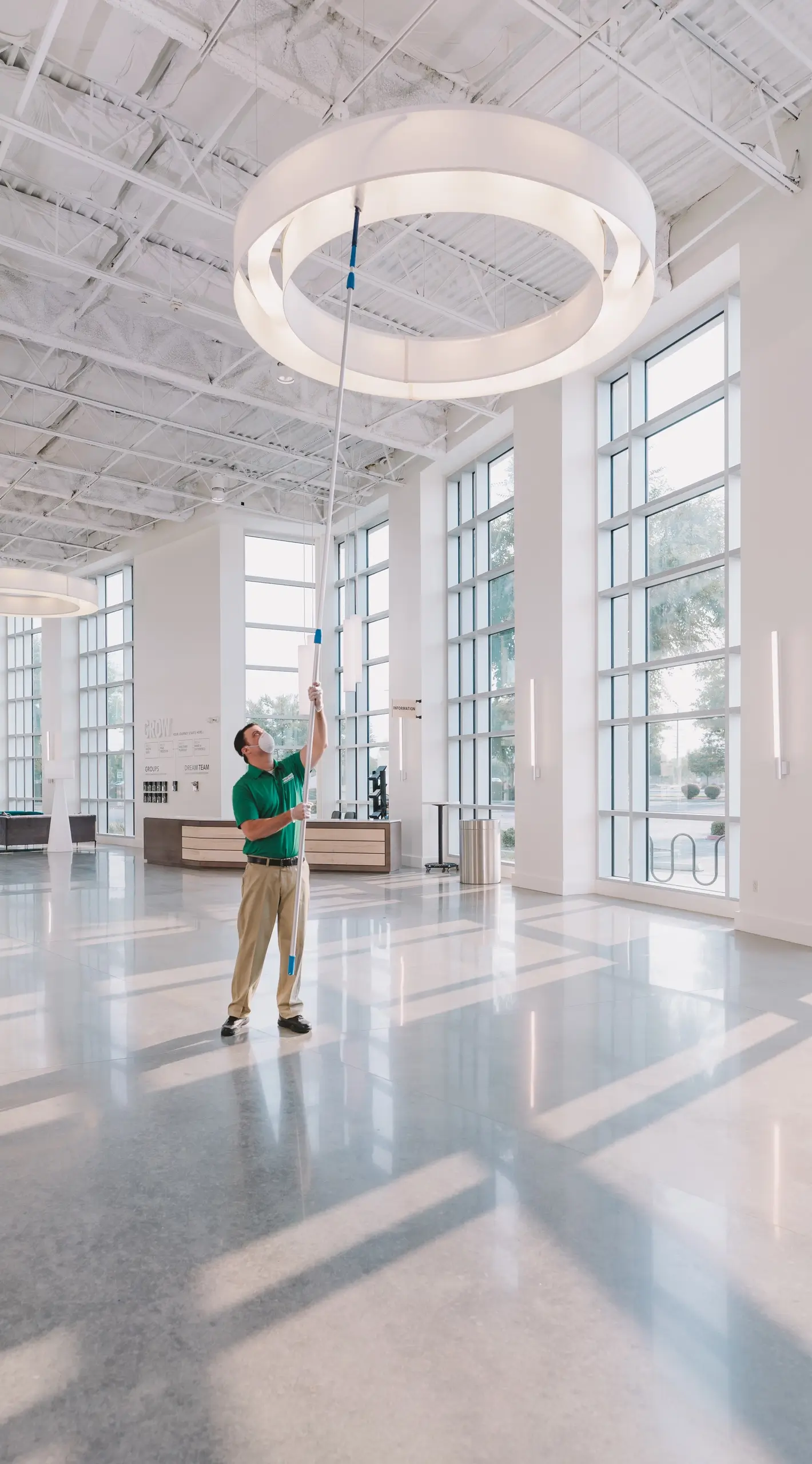 professional commercial cleaner dusting high ceiling lamp in a lobby early during sunrise
