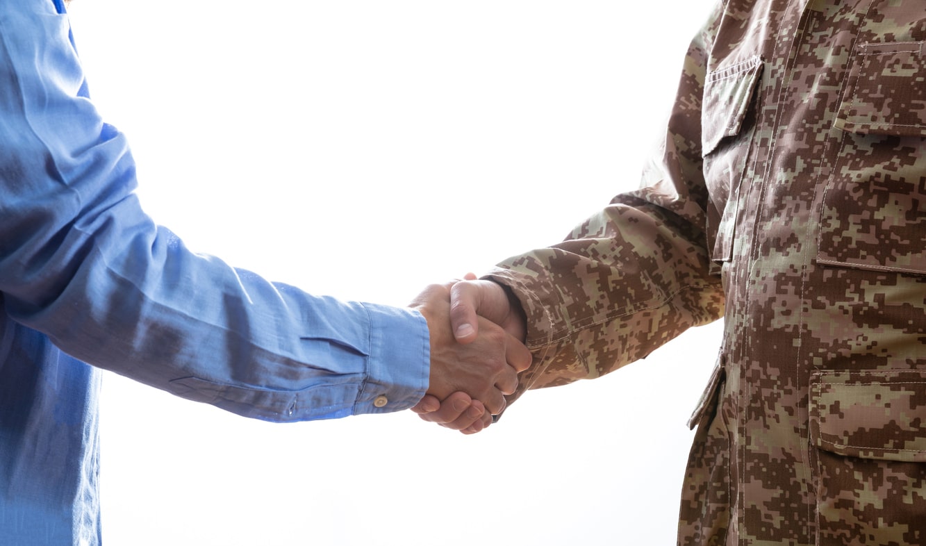 A man shaking hands with a veteran in a camouflage jacket
