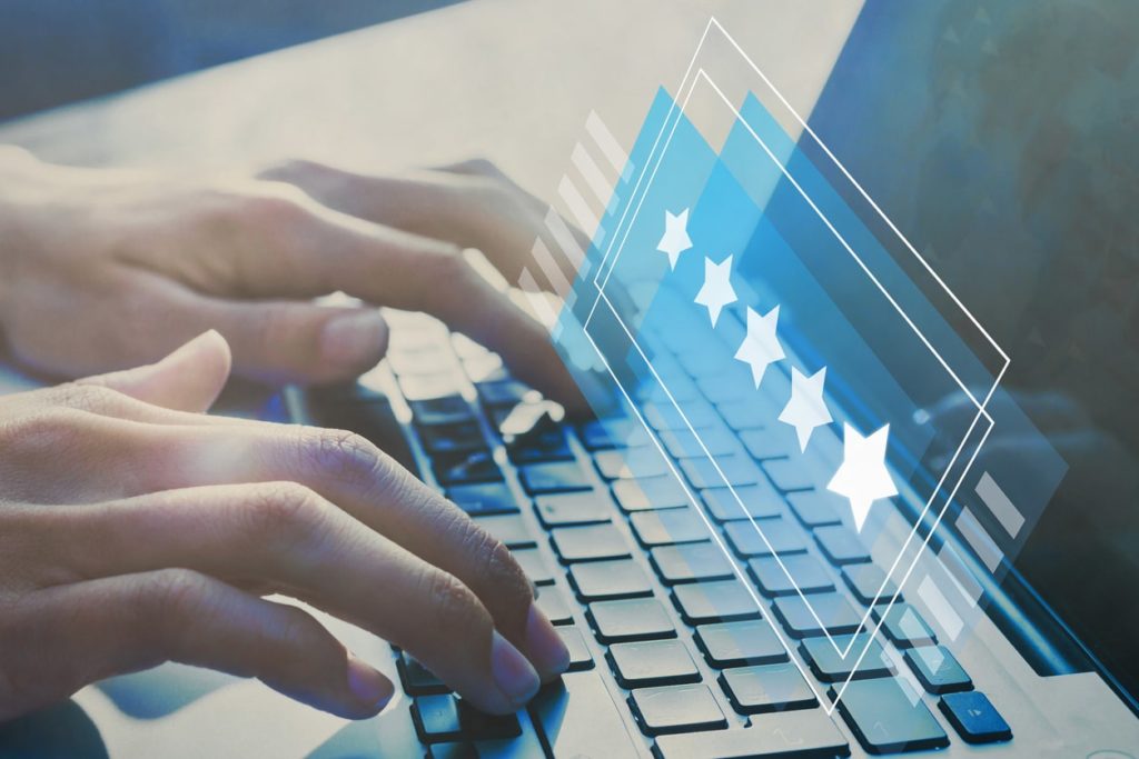 Hands over a laptop writing a review with a graphic of 5 stars hovering over the keyboard