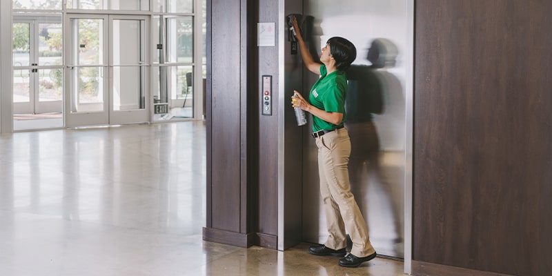 cleaning professional disinfecting an elevator doorway in a lobby area