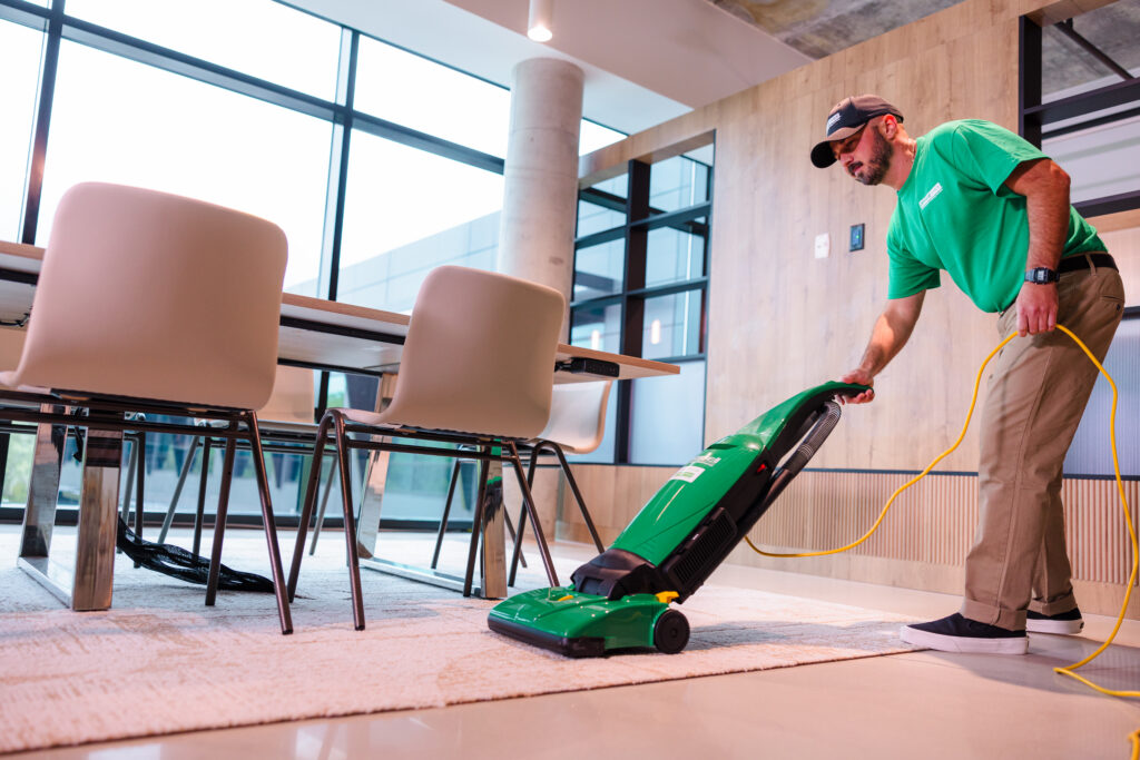 Office Pride cleaner vacuuming carpet around conference room chairs